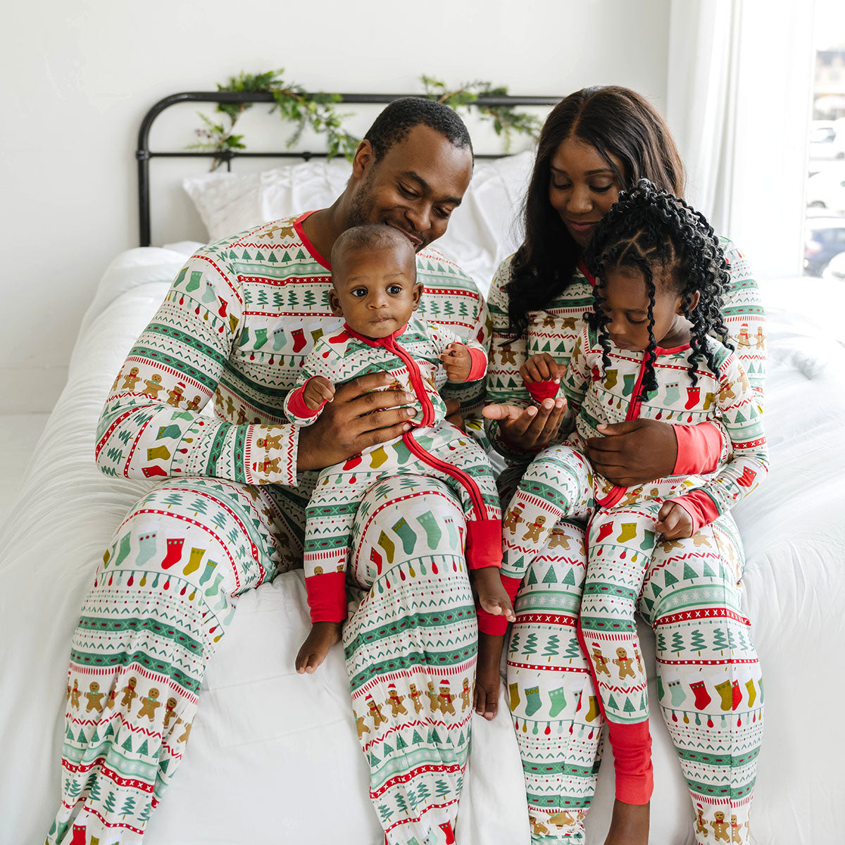 Family of four wearing matching Fair Isle pajamas. Mom is wearing Fair Isle women's pajama pants and top and Dad is matching wearing men's Fair Isle men's top and matching pants. Children are wearing Fair Isle pjs in zippy and two piece styles