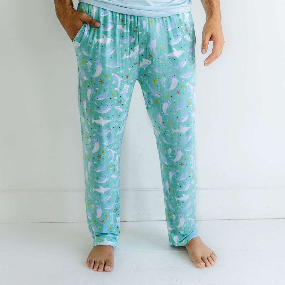 Image of male model wearing shark printed pajama pants. This print features hammerhead and great white sharks on an aqua background.