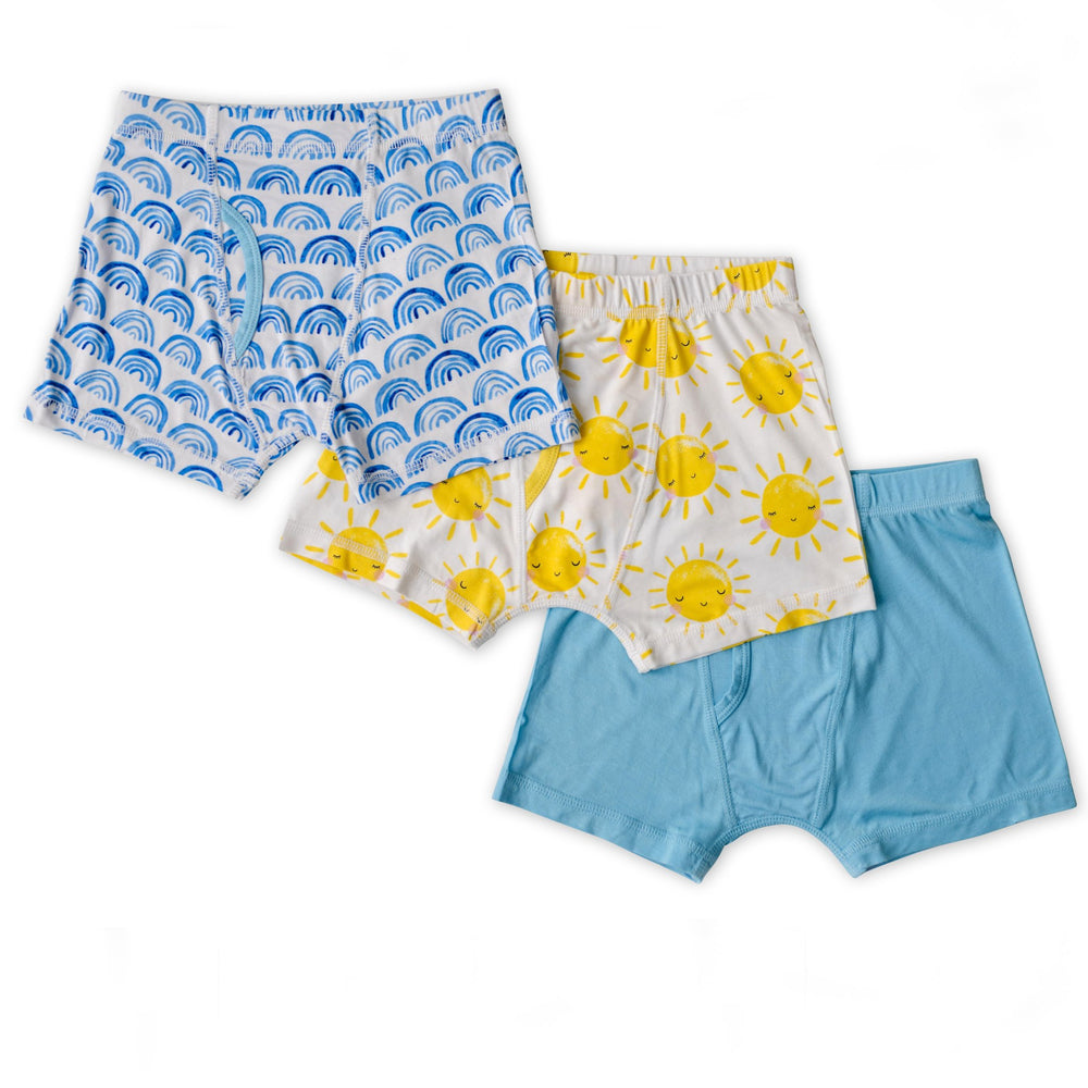 Flat lay image of 3 sets of boys boxer brief underwear. One blue rainbows print, followed by one yellow smiling sunshine print, followed by one solid sky blue print. 