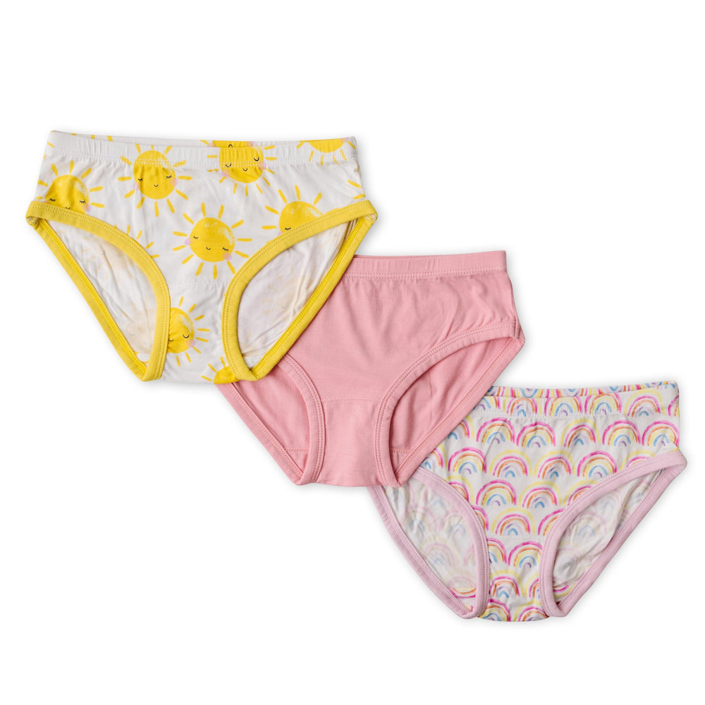 Flat lay image of 3 sets of girls brief underwear. One yellow smiling sunshine printed style, followed by one solid bubblegum pink style, followed by one pastel pink rainbows printed style.