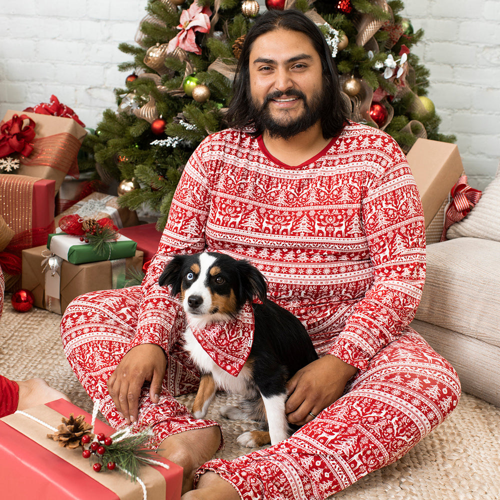 Man and his dog wearing matching Reindeer Cheer pajamas. Dad is wearing men's Reindeer Cheer pajama top and matching pants, his dog is wearing a Reindeer Cheer bandana. 