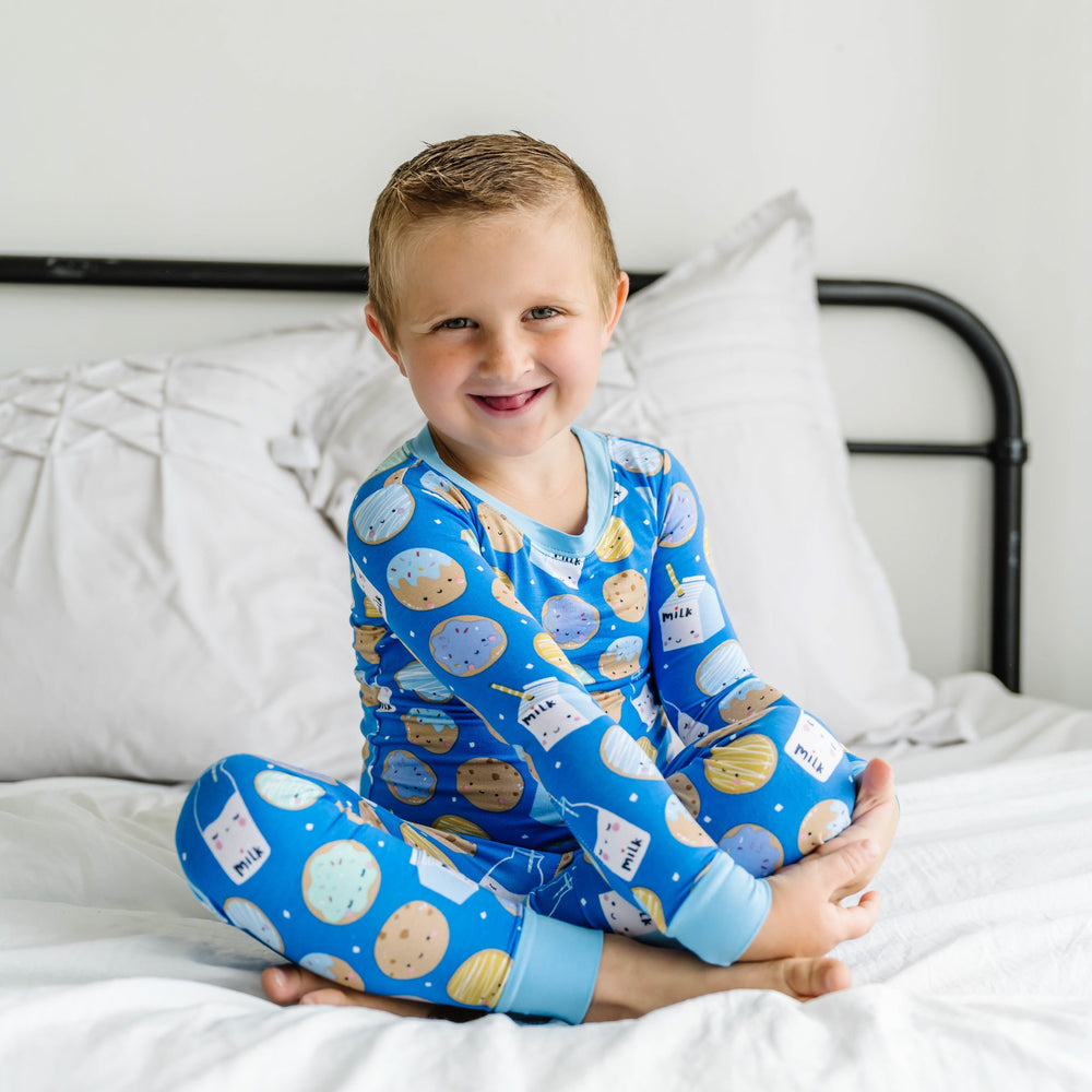 Image of little boy wearing a two-piece pajama set in cookies and milk set. This print features milk cartons, colorful sprinkled cookies, and chocolate chip cookies that sit upon a blue background with sky blue trim.