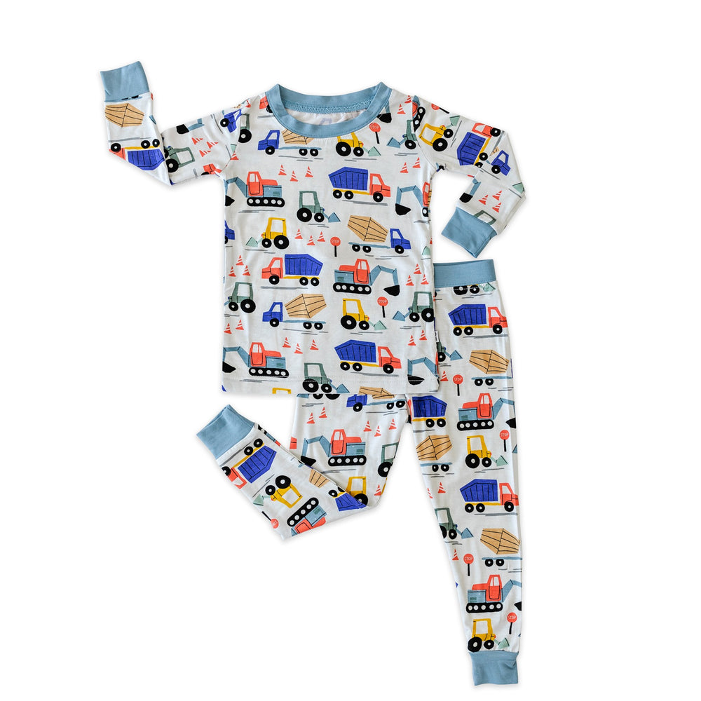 Flat lay shot of Construction printed pajamas. This print features utility trucks and tractors on a white background with sky blue trim accents.