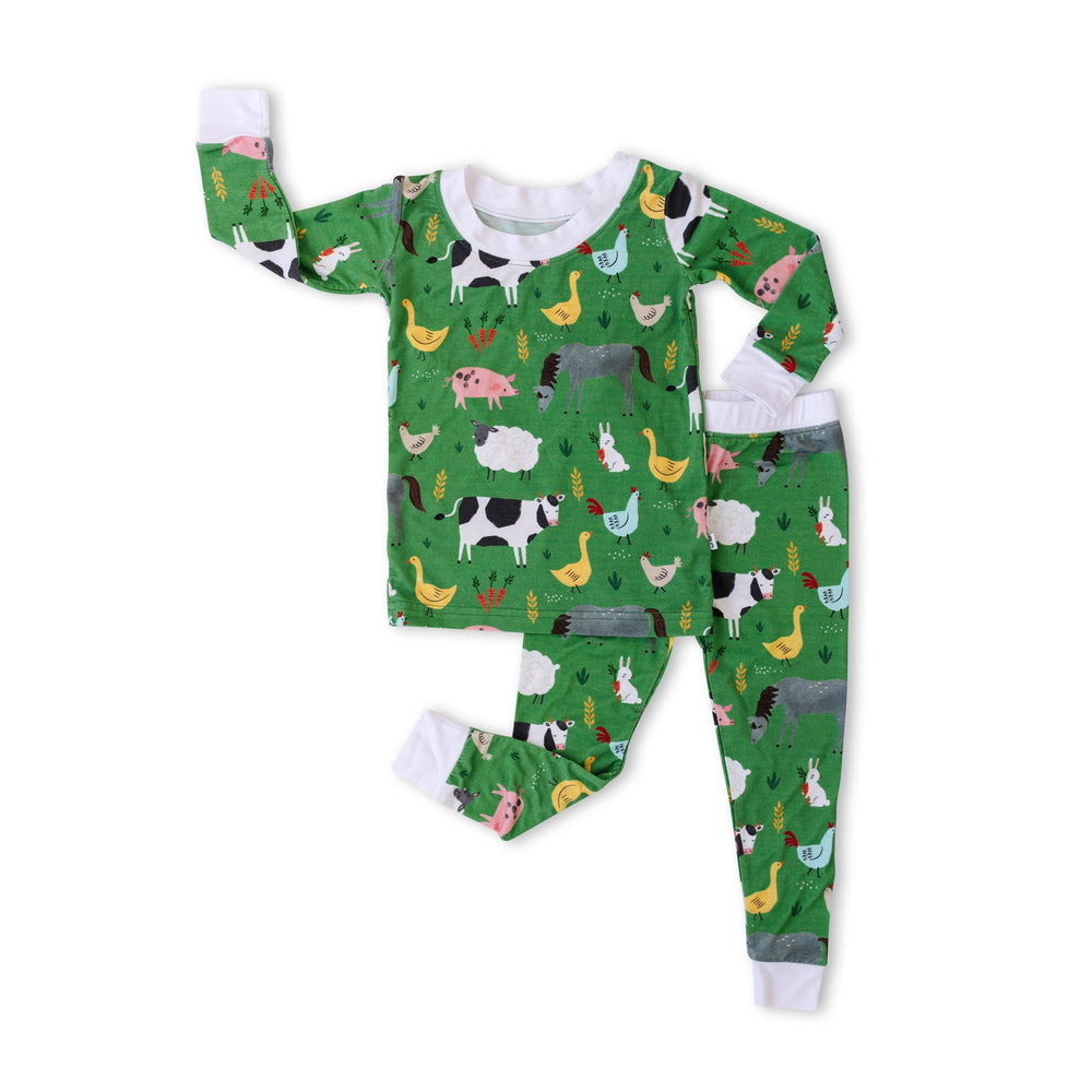 Flat lay image of two-piece pajama set in farm animals print. This print includes a green background with white trim details. The farm animals featured on this print include cows, pigs, ducks, sheep, pigs, chickens, and bunnies.