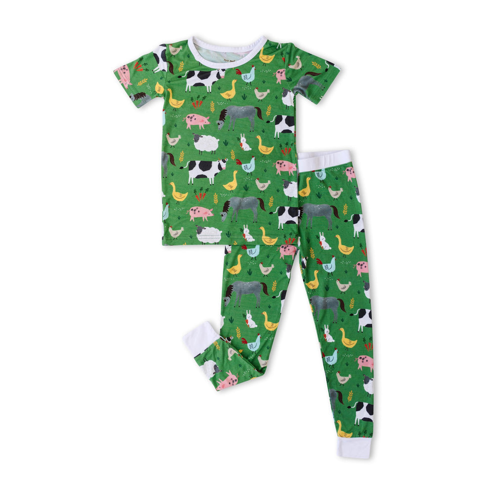 Flat lay image of a two-piece short sleeve pajama set in green farm animals print. This print includes a green background with white trim details. The farm animals featured on this print include cows, pigs, ducks, sheep, pigs, chickens, and bunnies.