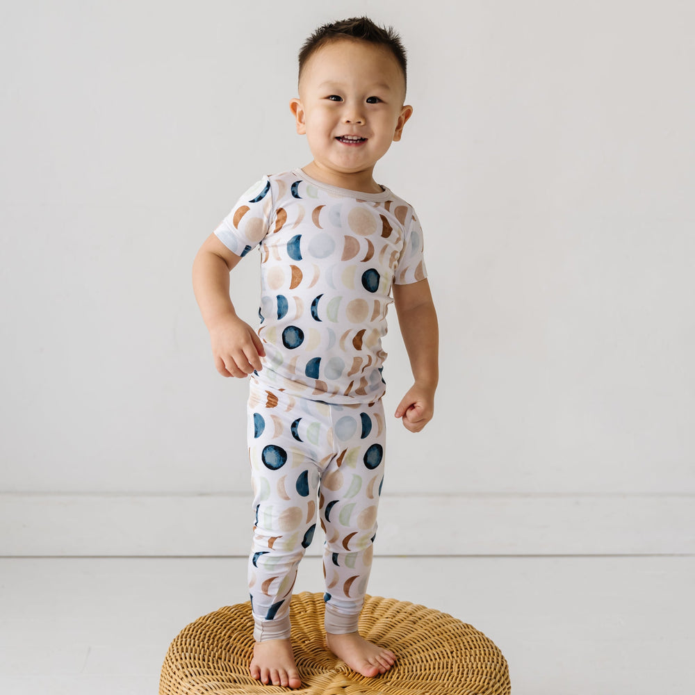 Image of a toddler in Luna Neutral printed pajamas. This print features phases of the moon in the sweetest shades of creams, tans, and navy watercolor in an all over repeat pattern.