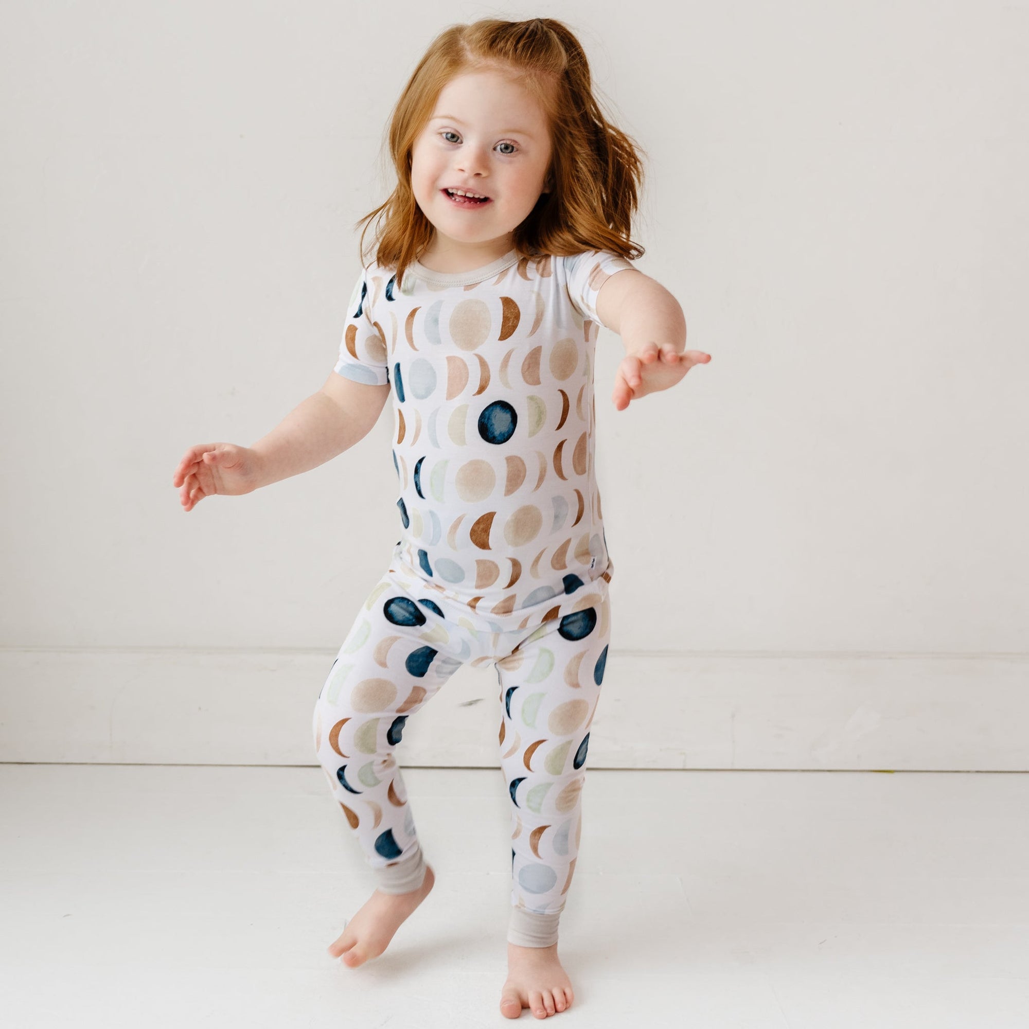 Image of a toddler in Luna Neutral printed pajamas. This print features phases of the moon in the sweetest shades of creams, tans, and navy watercolor in an all over repeat pattern.