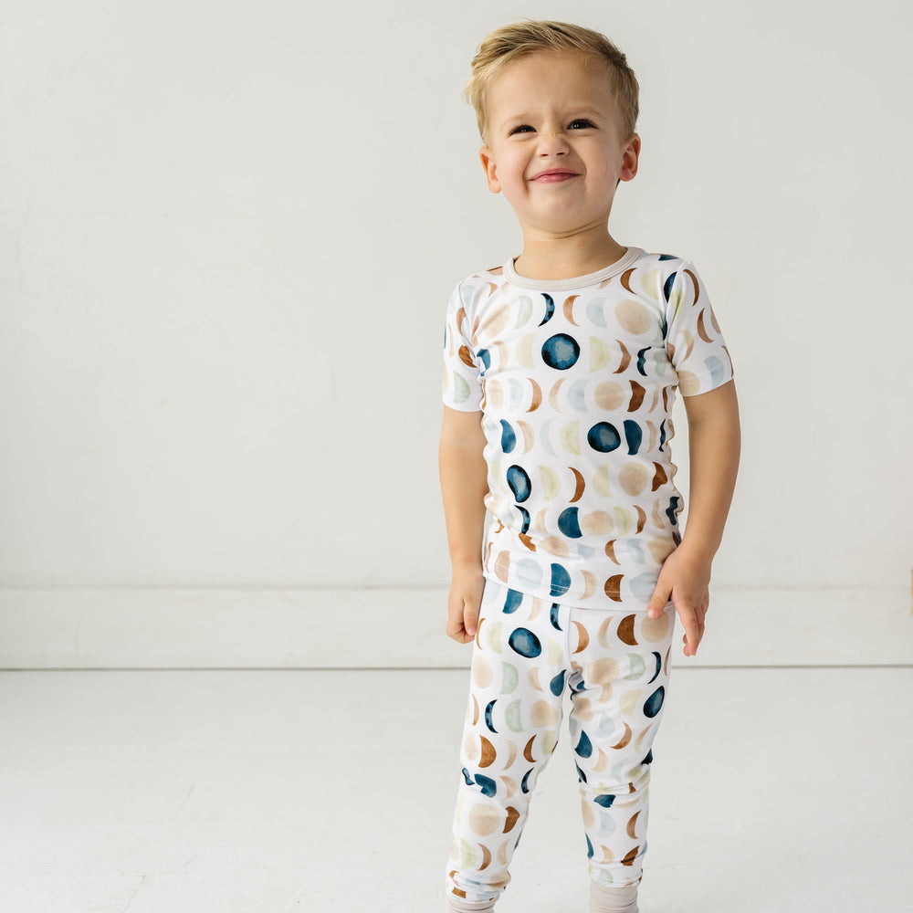 Image of a toddler in Luna Neutral printed pajamas. This print features phases of the moon in the sweetest shades of creams, tans, and navy watercolor in an all over repeat pattern.