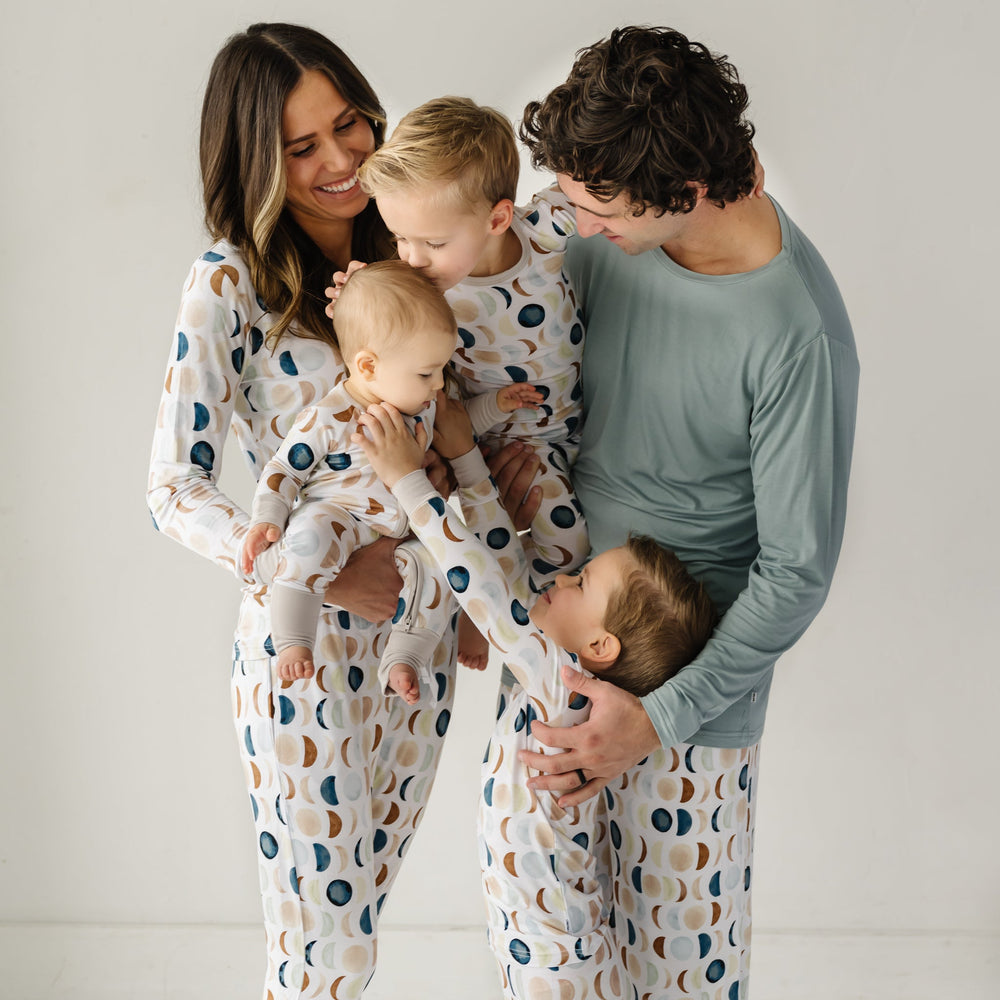 Image of a family of five of a mother, father, and three young children in matching Luna Neutral printed pajamas. This print features phases of the moon in the sweetest shades of creams, tans, and navy watercolor in an all over repeat pattern.
