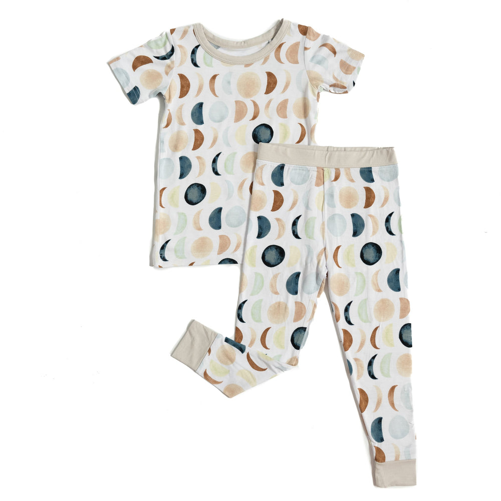 Flat lay image of short sleeve and pant set pajamas in Luna Neutral print. This print features phases of the moon in the sweetest shades of creams, tans, and navy watercolor in an all over repeat pattern.