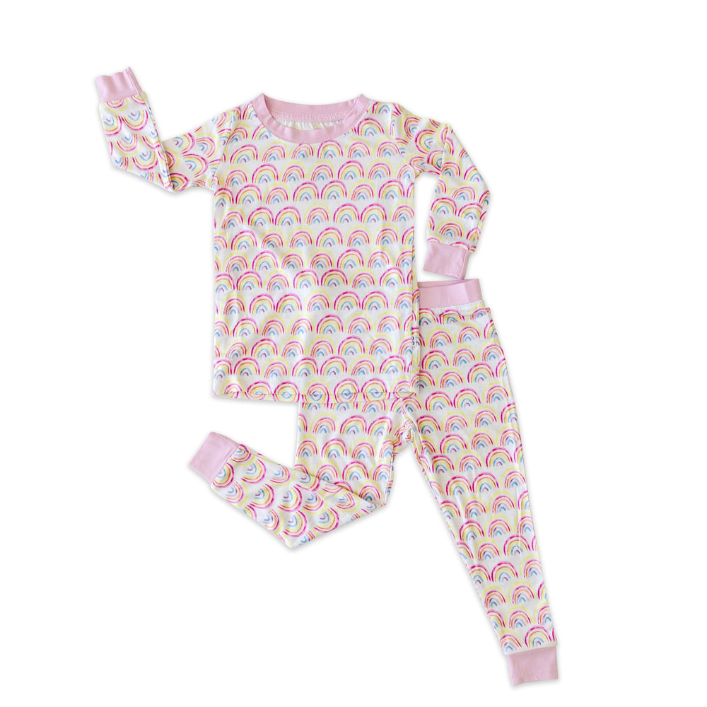 Flat lay image of two-piece pajama set in rainbows set. This print features multicolored rainbows that sit upon a white background with light pink accent trim.