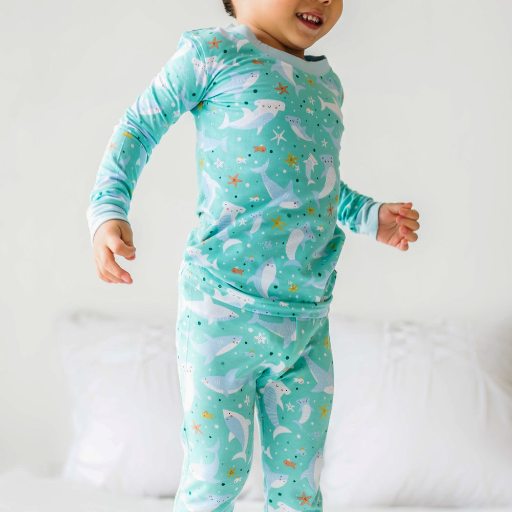 Zoomed in image of two-piece pajama set in shark print. This print includes hammerhead and great white sharks, featured on an aqua background with a light blue trim.
