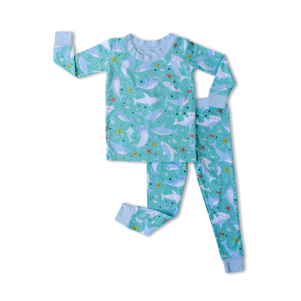 Flat lay image of two-piece pajama set with sharks print. This print includes hammerhead and great white sharks, featured on an aqua background with a light blue trim. 