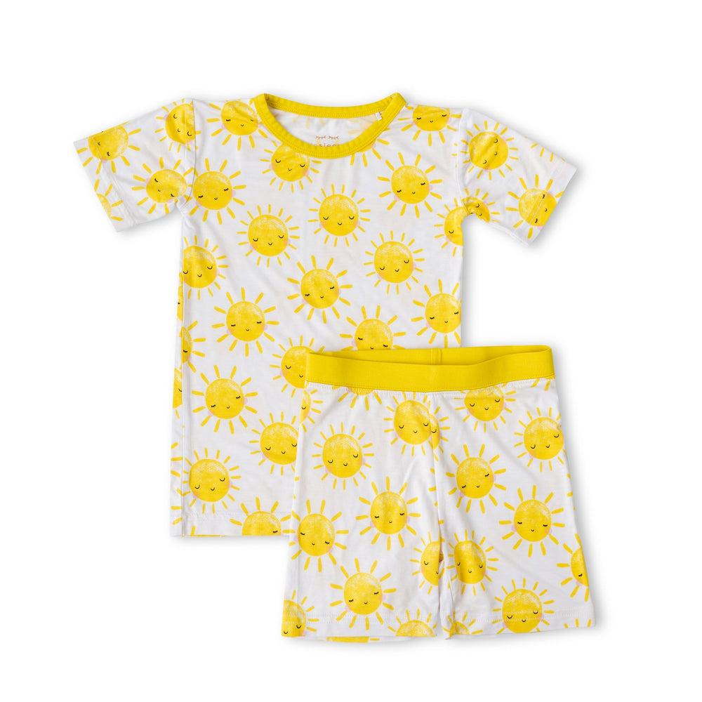 Flat lay image of two-piece short sleeve and shorts pajama set in Sunshine print. The yellow smiling suns on this print sit upon a white background, accented with yellow trim.