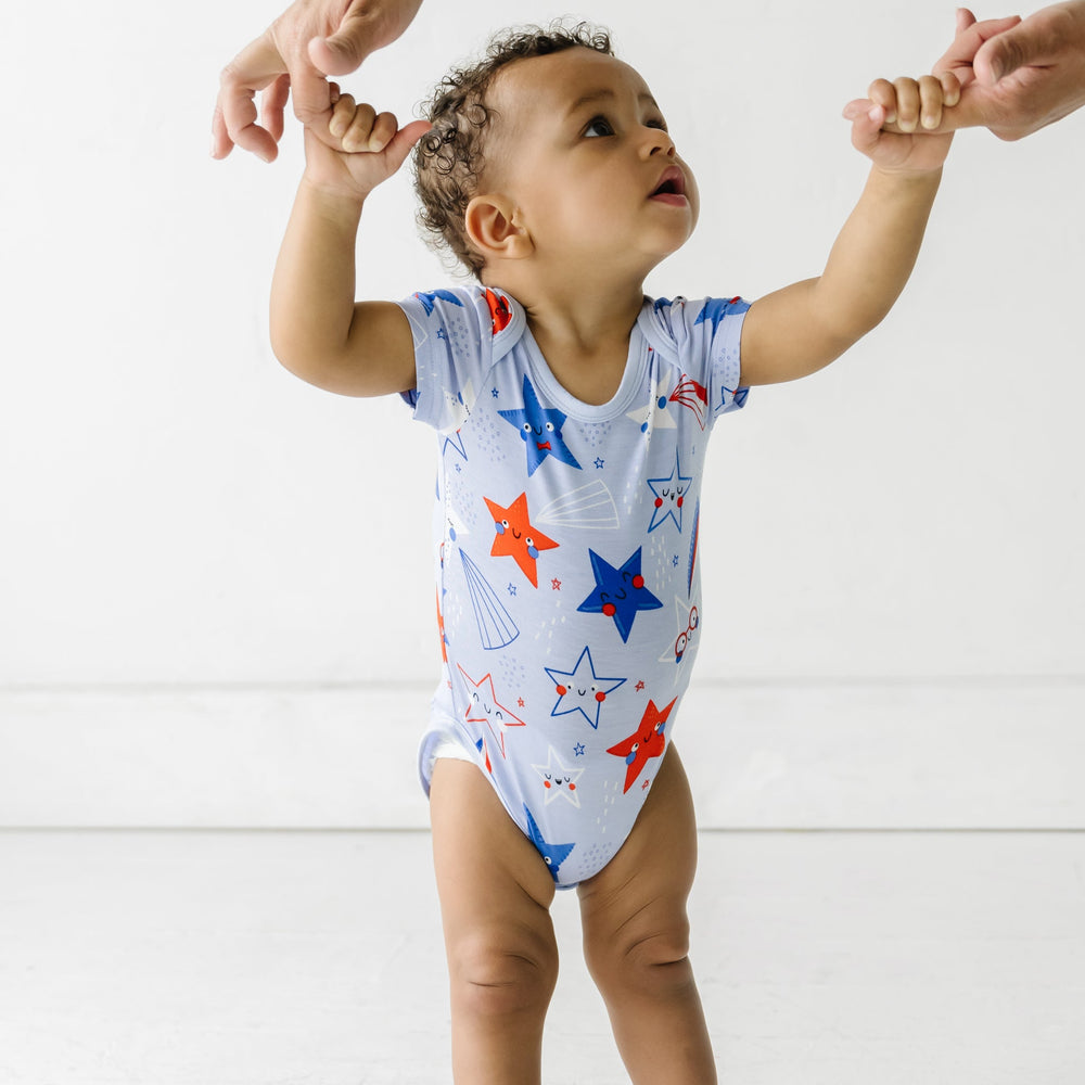 Click to see full screen - Child being held up by his parents wearing a Blue Stars and Stripes short sleeve bodysuit