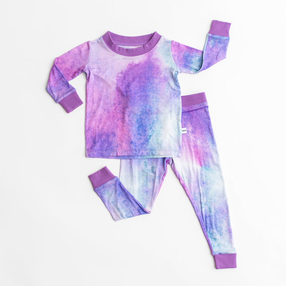 Flat lay image of two-piece pajama set in purple watercolor print. This watercolor print includes shades of purple, hues of white, and the slightest hint of blue. It is accented with purple trim. 