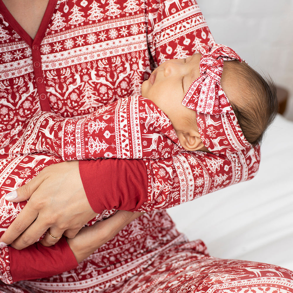 Close up image of a child swaddled in a Reindeer Cheer swaddle and headband set in their mother's arms. Their mother is wearing Reindeer Cheer women's pajama top and pants.