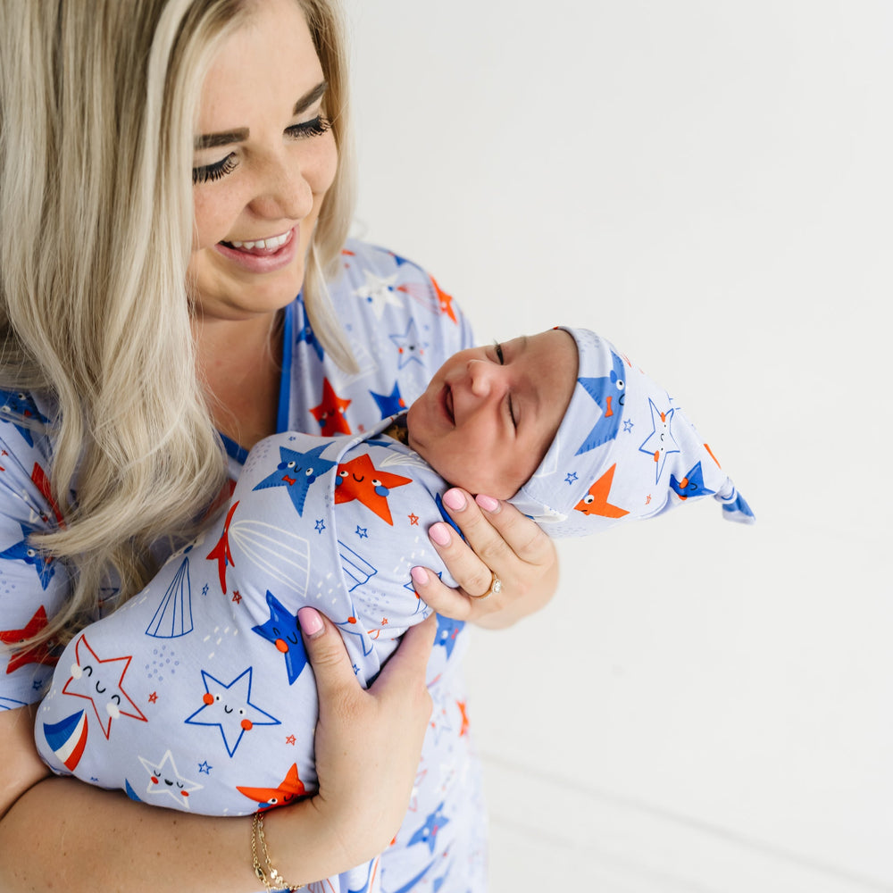 Mother holding her newborn swaddled in a Blue Stars and Stripes printed swaddle and hat set