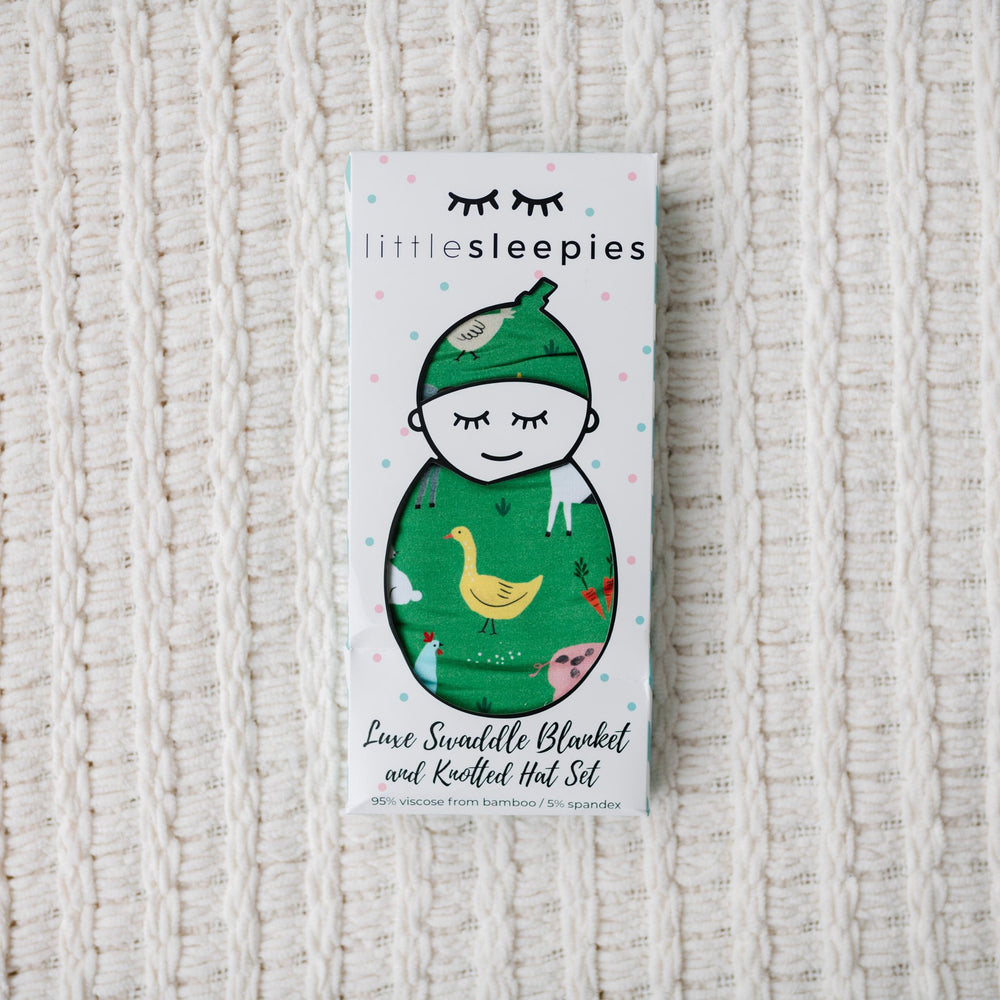 Image of green farm animal printed swaddle and hat set in Little Sleepies packaging. 