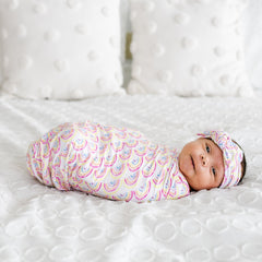 Image of infant girl wearing rainbow printed swaddle and headband set.