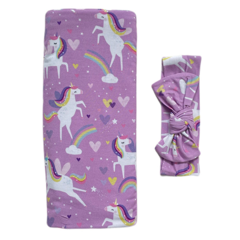 Click to see full screen - Flat lay image of swaddle and headband set in Sienna's Unicorns print. Flying unicorns with rainbow-colored manes gallop across a purple background with hearts, stars, and rainbows in this magical print.