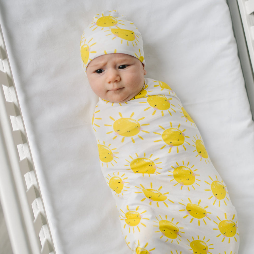 Image of infant baby wearing swaddle and hat set with printed yellow smiling suns