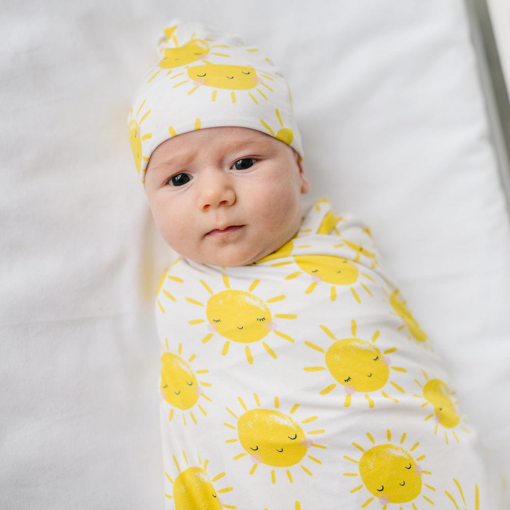 Click to see full screen - Image of infant baby wearing swaddle and hat set with printed yellow smiling suns