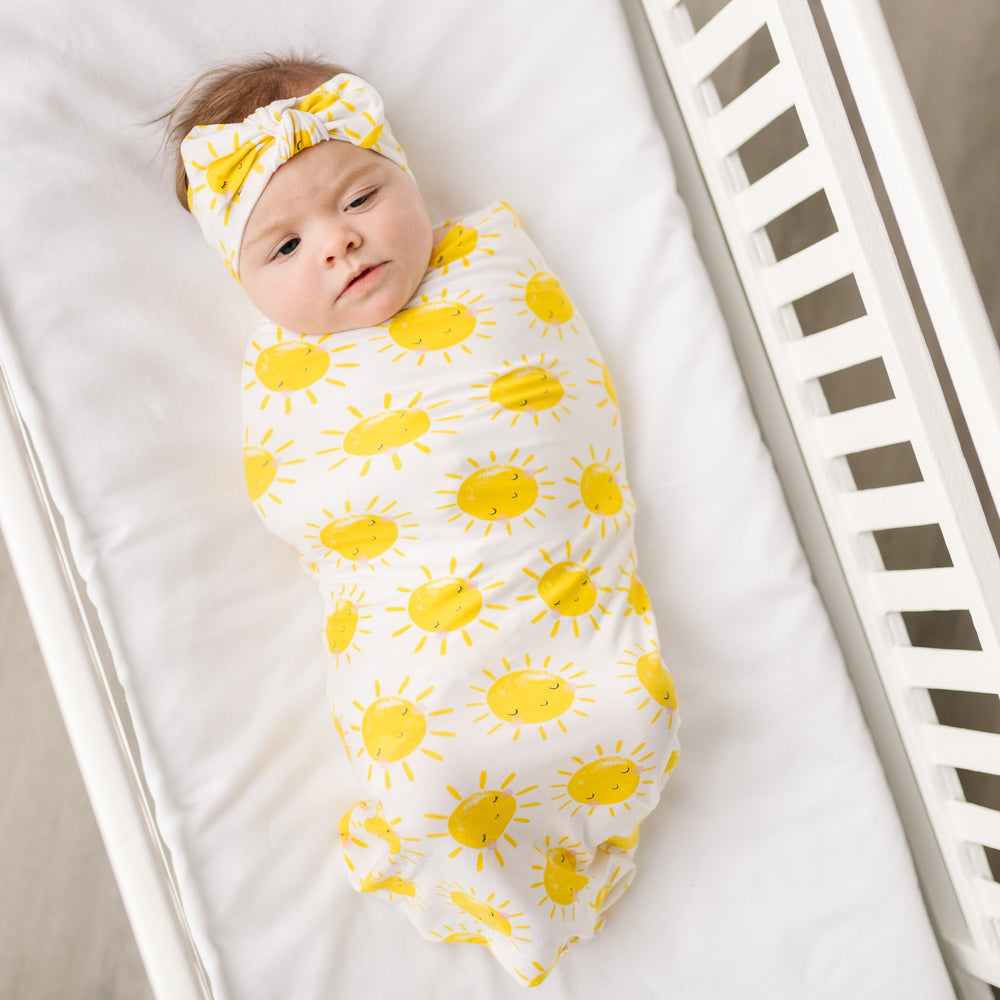 Image of infant baby wearing swaddle and headband set with printed yellow smiling suns