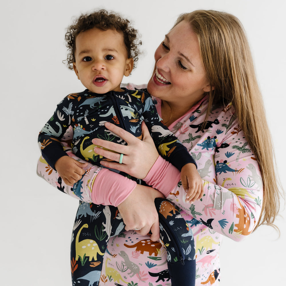 Click to see full screen - Mother and son wearing coordinating Jurassic Jungle pajamas. Son is wearing a Navy Jurassic Jungle printed zippy. Mom is wearing Pink Jurassic Jungle in women's pants and top.  