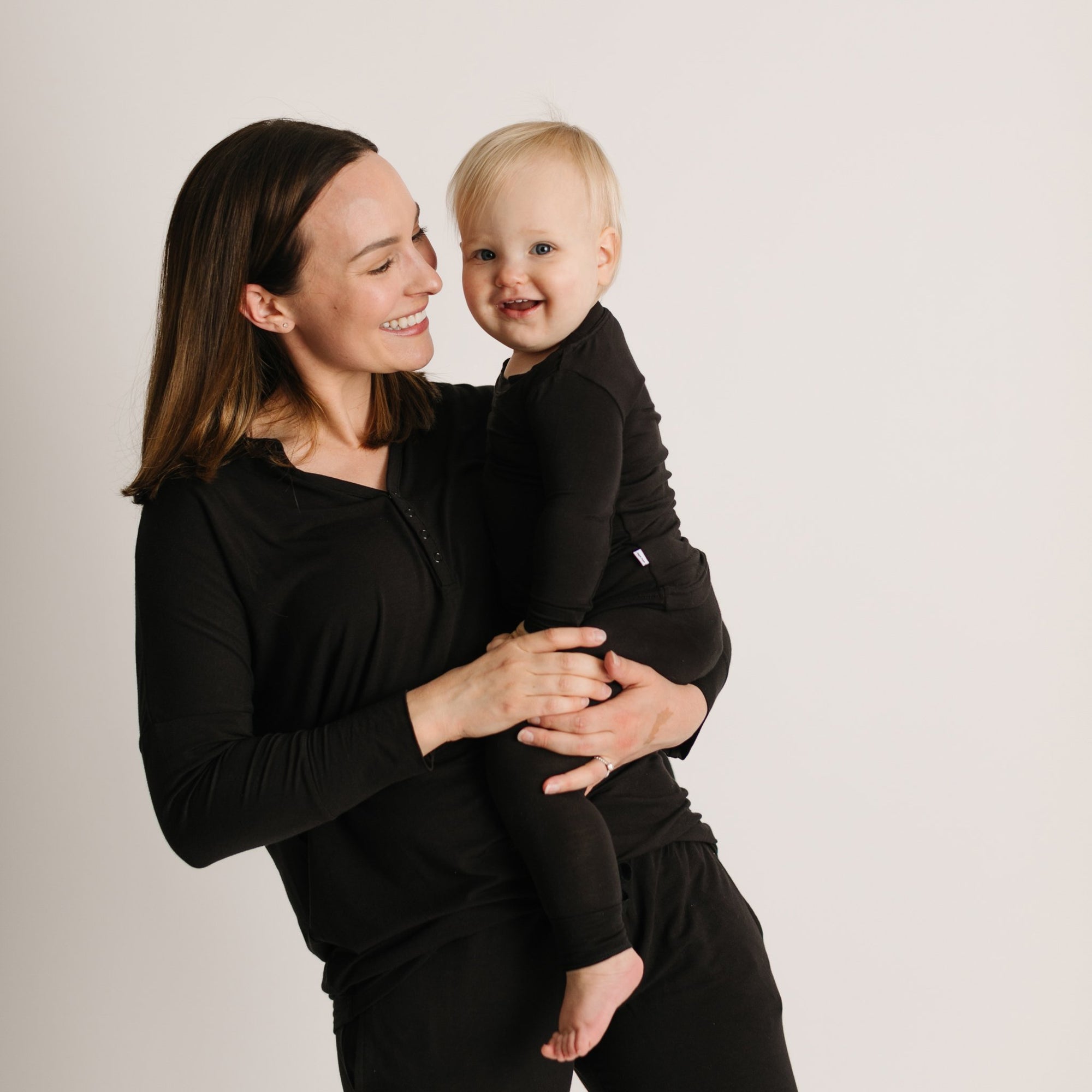 Mom and daughter both wearing solid black pajamas. Mom is holding her daughter in the photo.