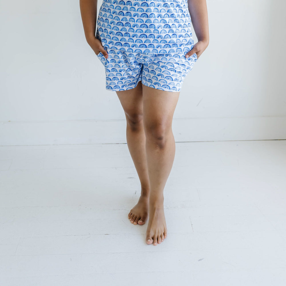 Image of female model wearing blue rainbow printed pajama shorts. This print sits on a white background with shades of blue rainbows and sky blue trim details.