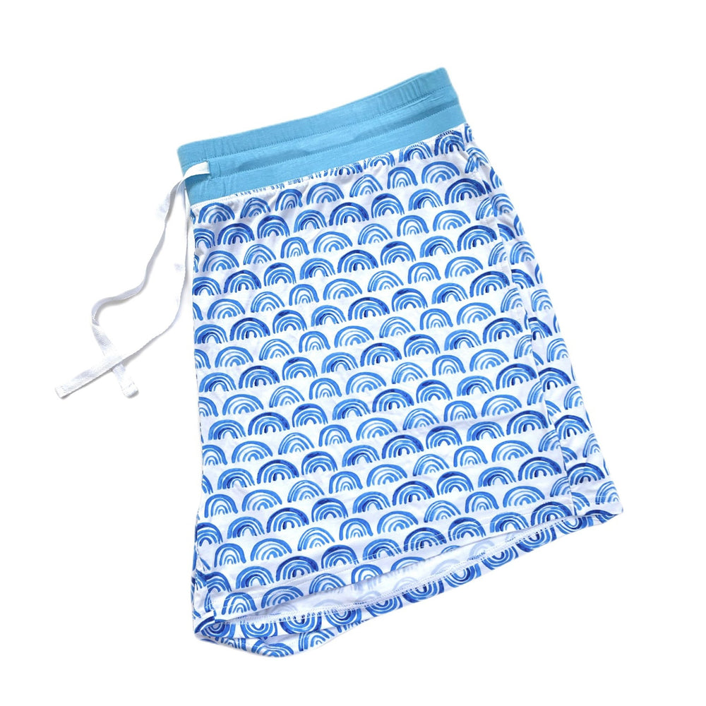 Flat lay image of women's pajama shorts in blue rainbows print. This print sits on a white background with shades of blue rainbows and sky blue trim details.
