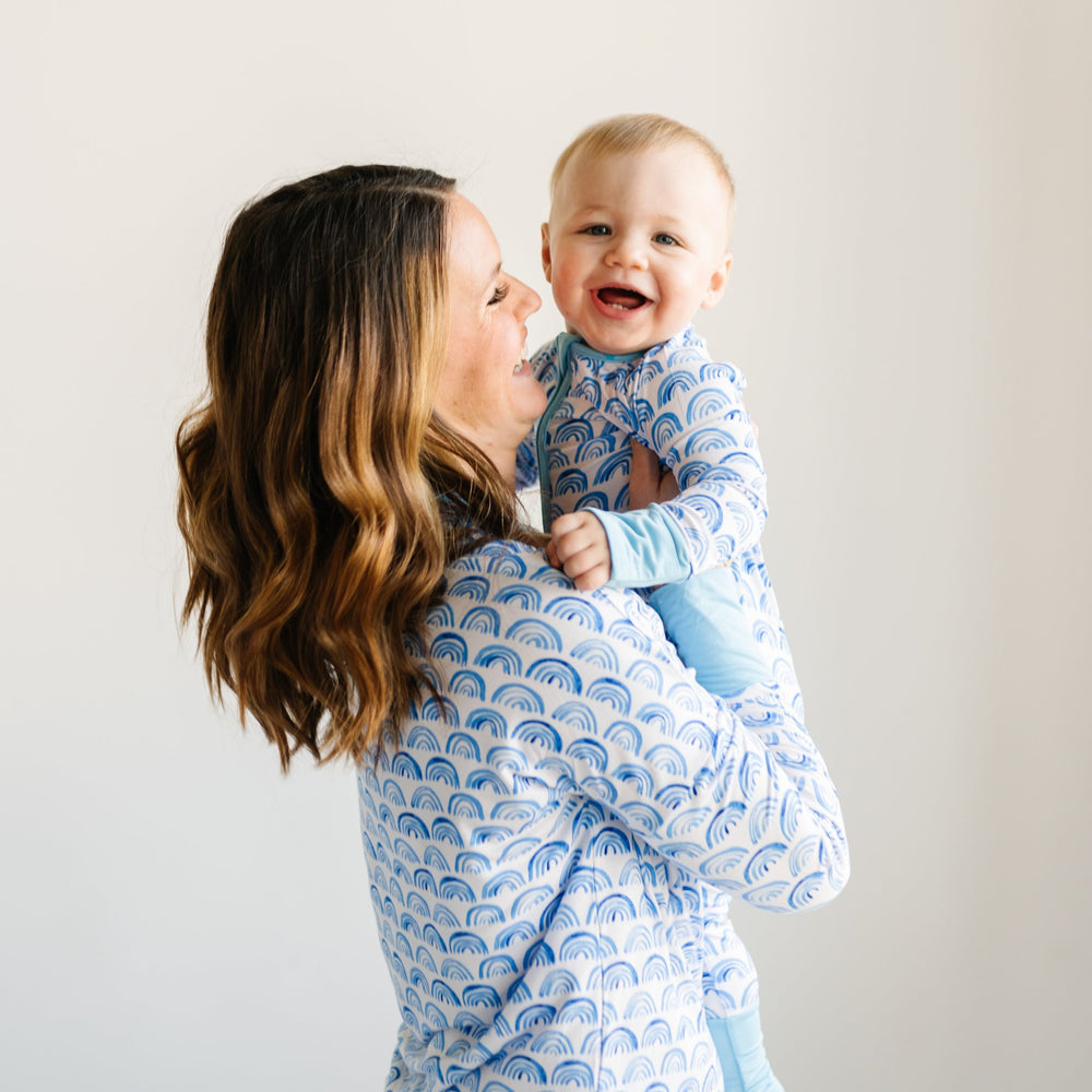 Click to see full screen - Image of mom and son wearing matching blue rainbow printed pajamas. This print sits on a white background with shades of blue rainbows and sky blue trim details.