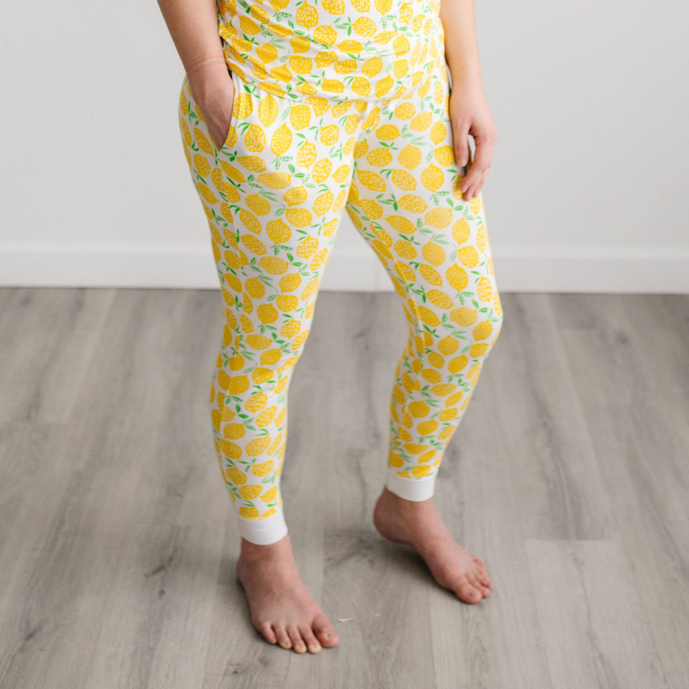 Image of female model wearing Lemons printed pajama pants. This print features vibrant pops of yellow fruit with green accents that sit upon a white background with white trim.