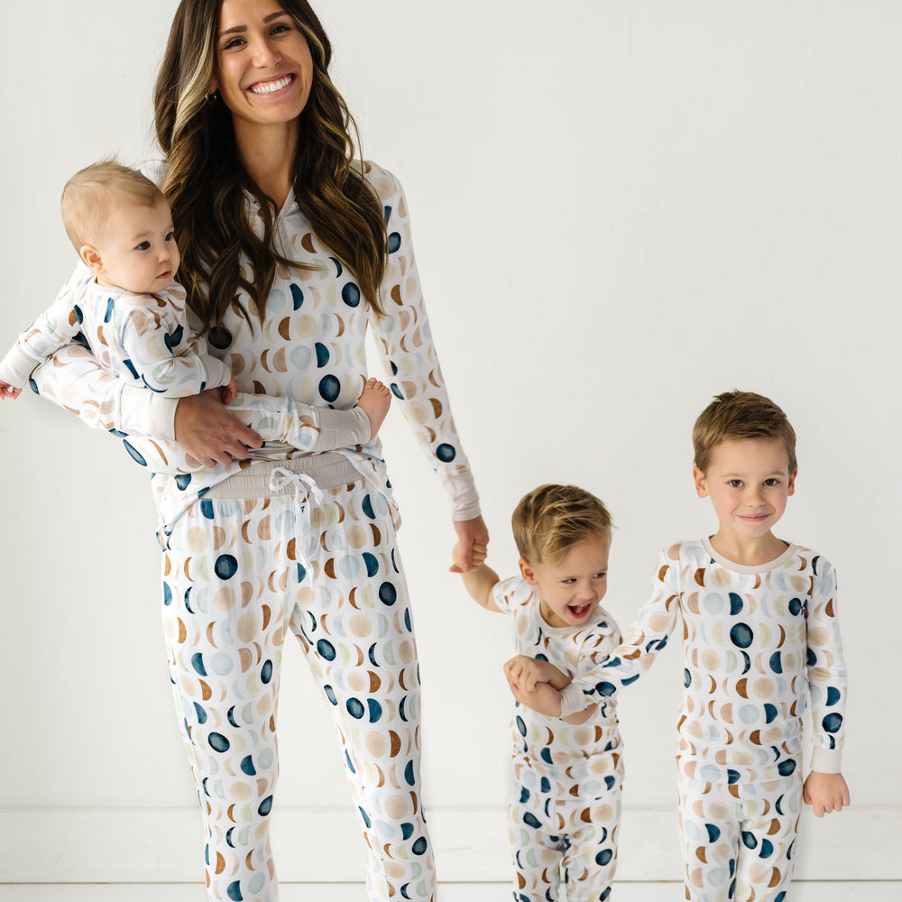 Image of a mother and three young children in matching pajama sets in Luna Neutral print. This print features phases of the moon in the sweetest shades of creams, tans, and navy watercolor in an all over repeat pattern.