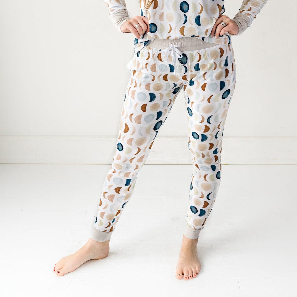 Click to see full screen - Cropped image of a woman wearing Luna Neutral printed pajama pants and matching long sleeve pajama top. This print features phases of the moon in the sweetest shades of creams, tans, and navy watercolor in an all over repeat pattern.
