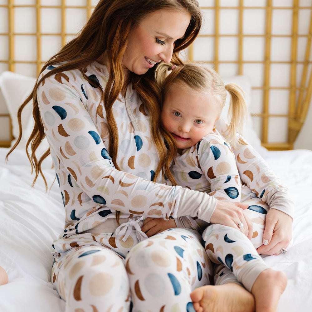 Image of a mother and daughter in matching pajama sets in Luna Neutral print. This print features phases of the moon in the sweetest shades of creams, tans, and navy watercolor in an all over repeat pattern.