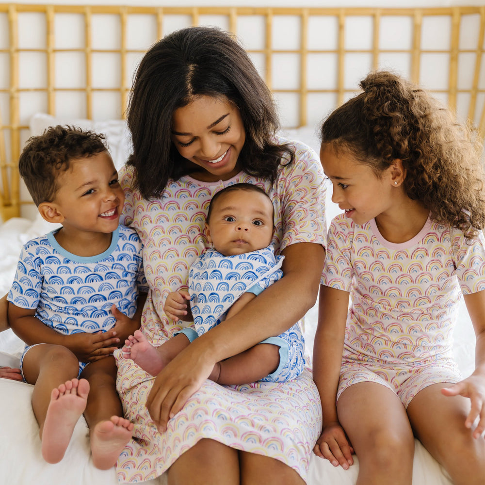 Image of mom and her 3 kids wearing matching rainbow printed pajamas.