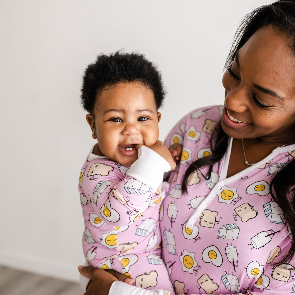 Click to see full screen - Image of mom and her daughter wearing matching Pink Breakfast Buddies printed pajamas. This print has a light pink background with white trim accents and the breakfast foods featured on this print include sunny side up eggs, toast, and milk.