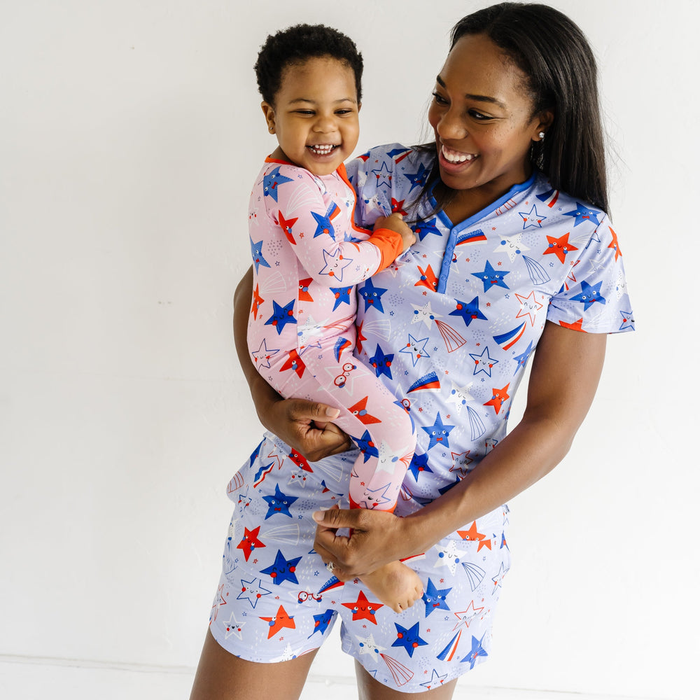Woman holding her child wearing Blue Stars and Stripes printed women's pajama shorts and matching women's pajama top. Child is coordinating in a Pink Stars and Stripes printed zippy