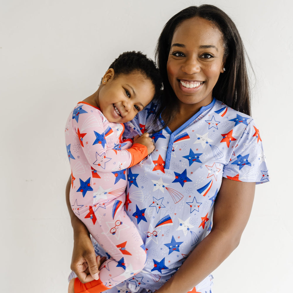Close up image of a woman holding her child wearing Blue Stars and Stripes printed women's pajama shorts and matching women's pajama top. Child is coordinating in a Pink Stars and Stripes printed zippy
