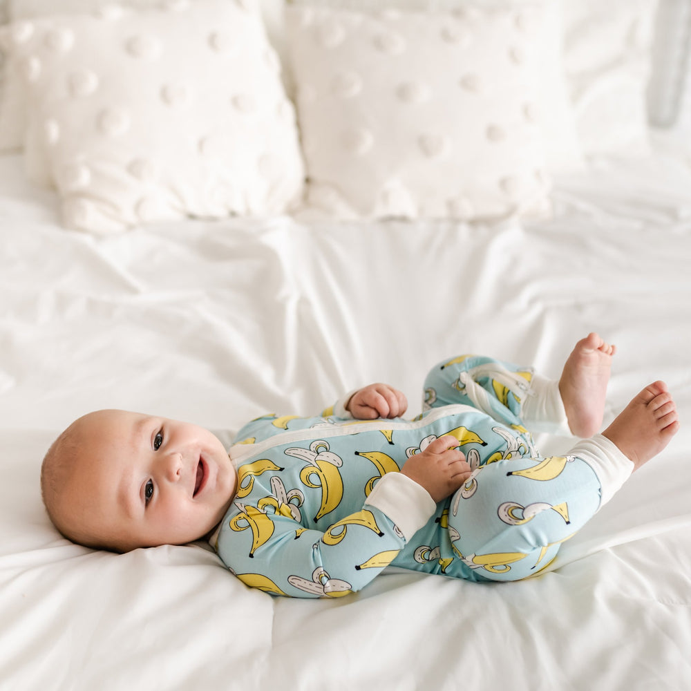 Click to see full screen - Baby boy wearing banana printed zip up romper. This banana printed zip up romper features a light blue background with pops of yellow and white trim accents on the collar, zip feature, sleeve cuffs, and pant cuffs.