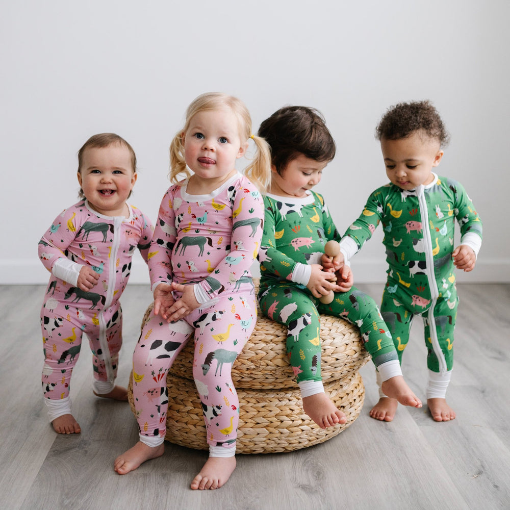 Image of 4 kids gathered around a stack of rattan poufs. The two little girls on the left are shown wearing pink farm animal printed pajamas, while the two boys on the left are shown wearing green farm animal printed pajamas. The animals featured on this 
