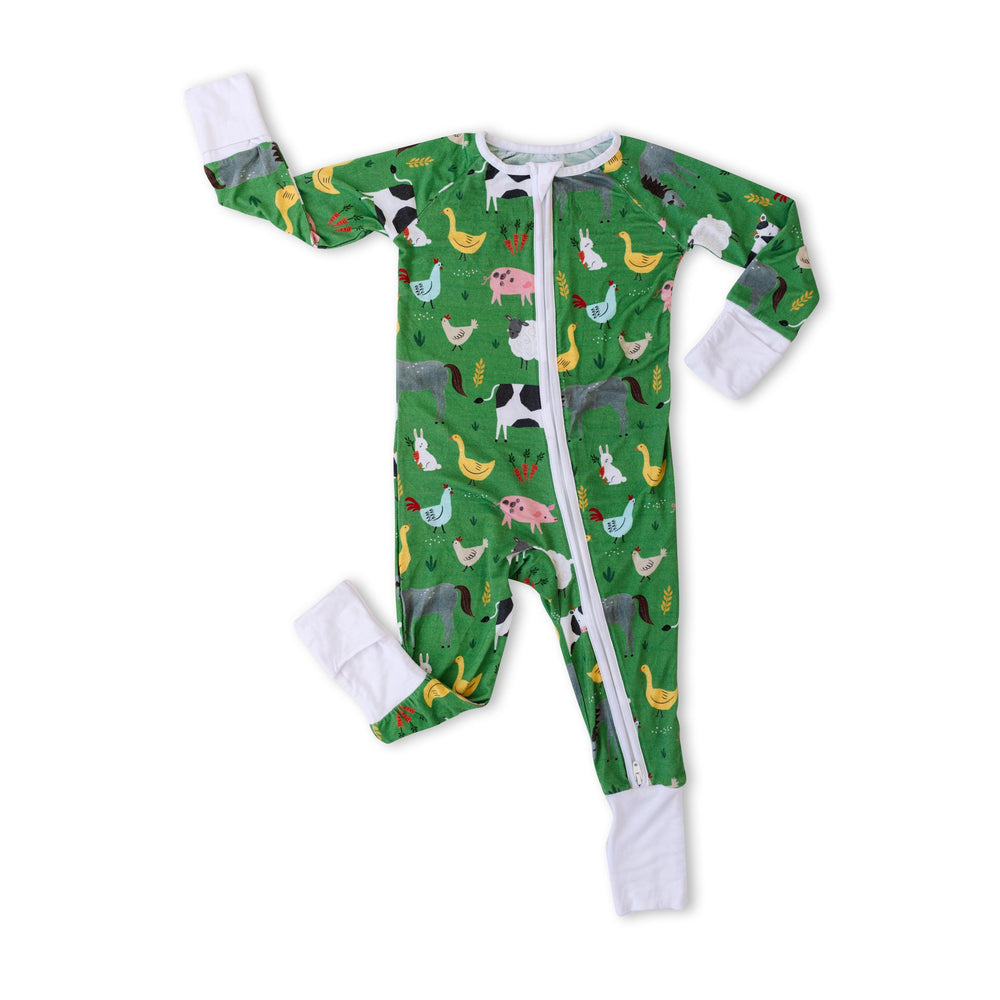 Flat lay image of zip up romper in green farm animals print. This print includes a green background with white trim details. The farm animals featured on this print include cows, pigs, ducks, sheep, pigs, chickens, and bunnies. 
