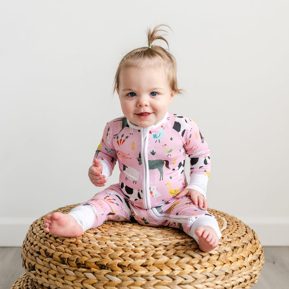 Click to see full screen - Child sitting on woven pouf wearing Pink Farm Animals zippy