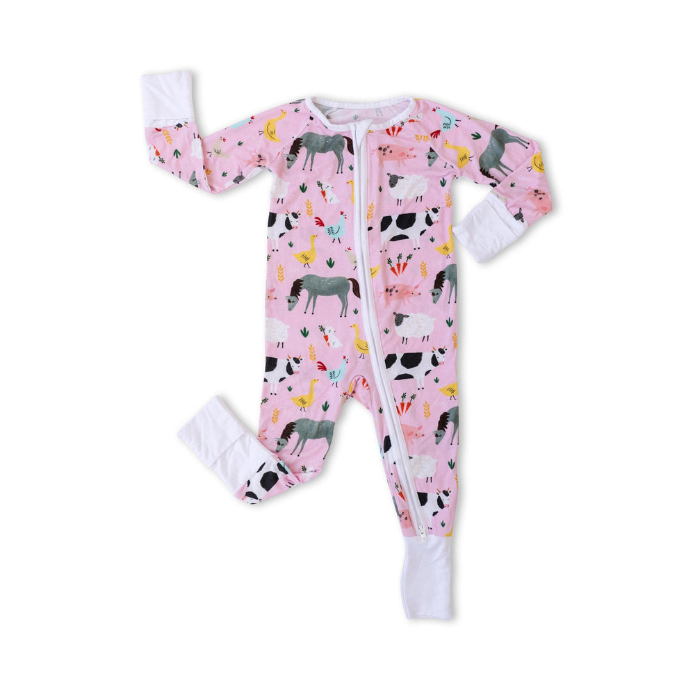 Click to see full screen - Flat lay image of zip up romper in pink farm animals print. This print includes a pink background with white trim details. The farm animals featured on this print include cows, pigs, ducks, sheep, pigs, chickens, and bunnies.