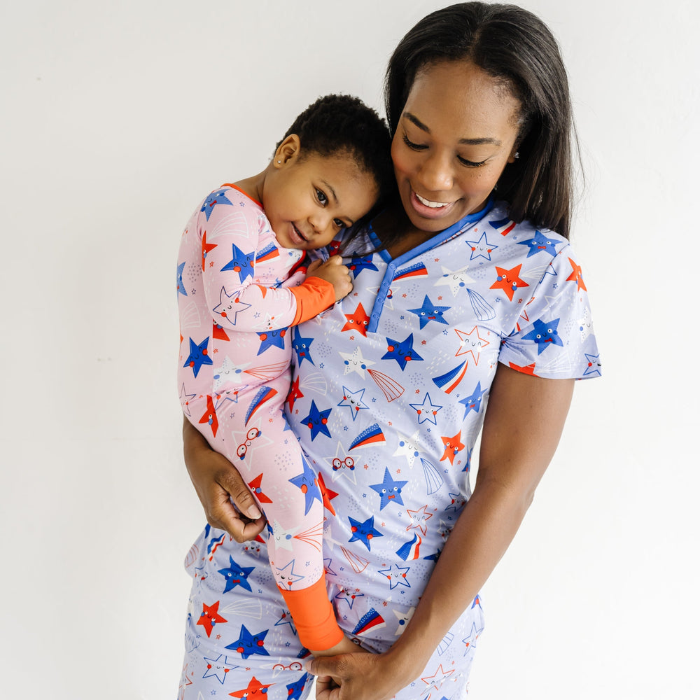 Woman holding her child wearing Blue Stars and Stripes printed women's pajama shorts and matching women's pajama top. Child is coordinating in a Pink Stars and Stripes printed zippy