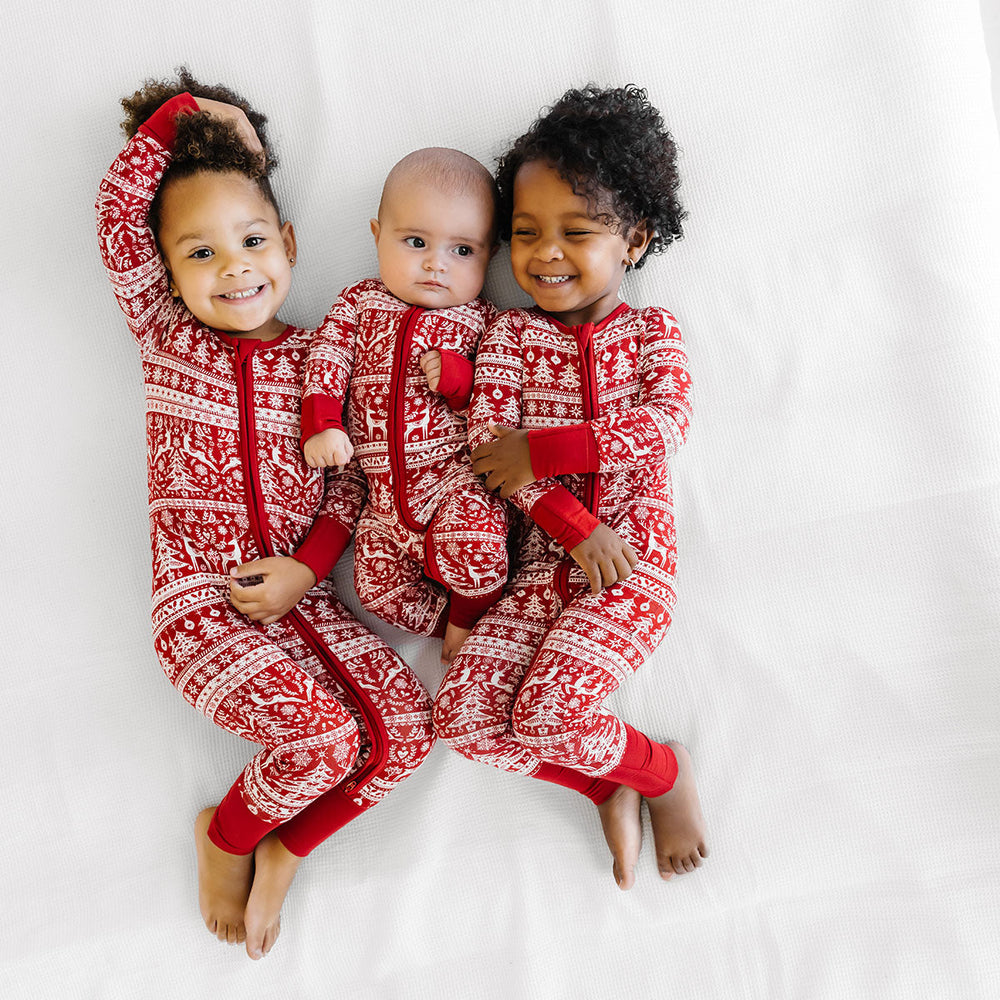 Three children laying on a bed wearing matching Reindeer Cheer zippies